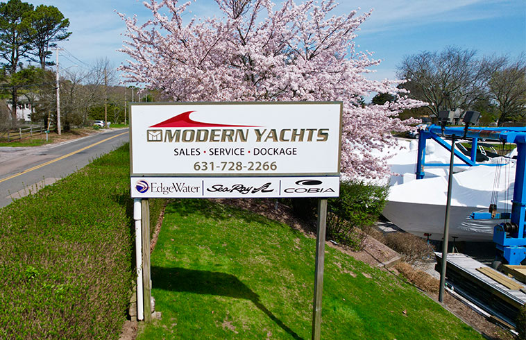  Aerial view of Modern Yachts signboard along a roadside, with blooming cherry trees and covered boats on lifts in the background.