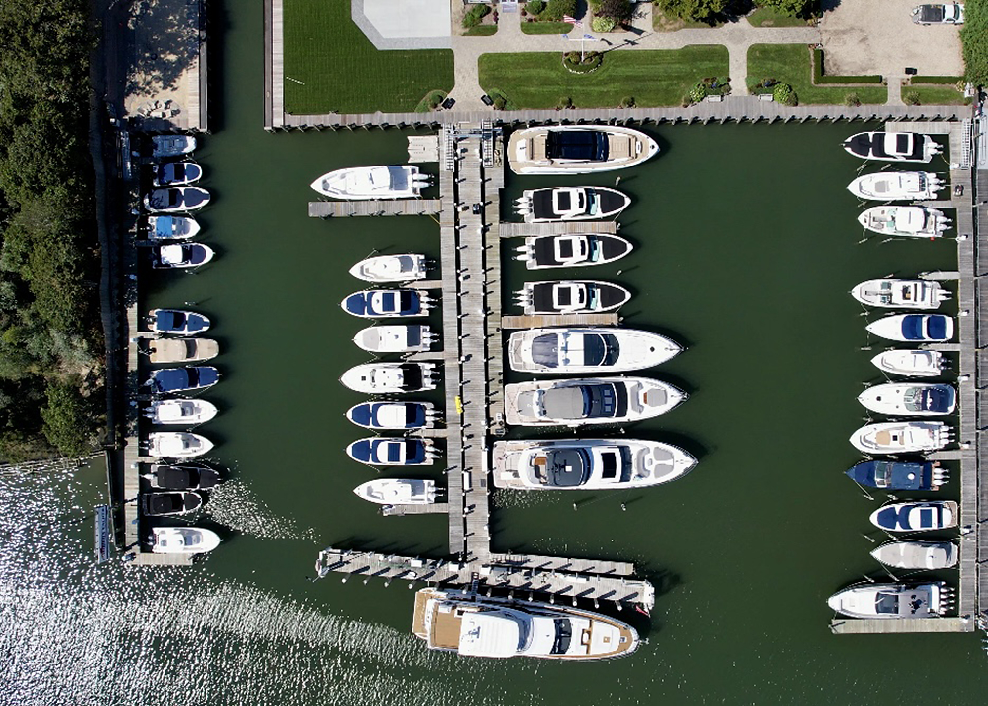 Top-down shot of a marina with neatly arranged boats docked in calm waters, casting clear shadows on the water surface.