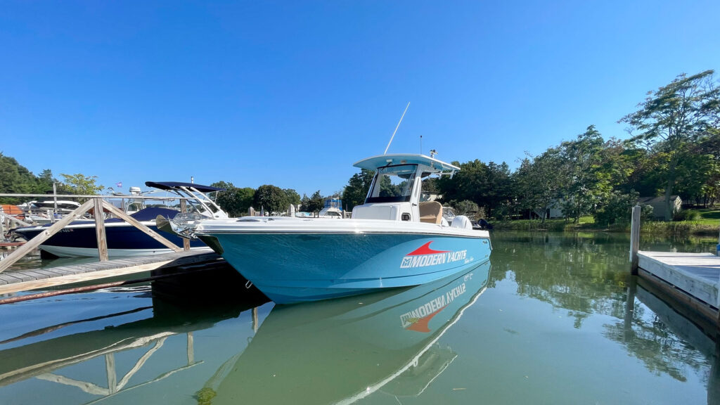 serene aqua-colored center console boat moored at a calm marina, with clear reflections on the water and greenery in the background.