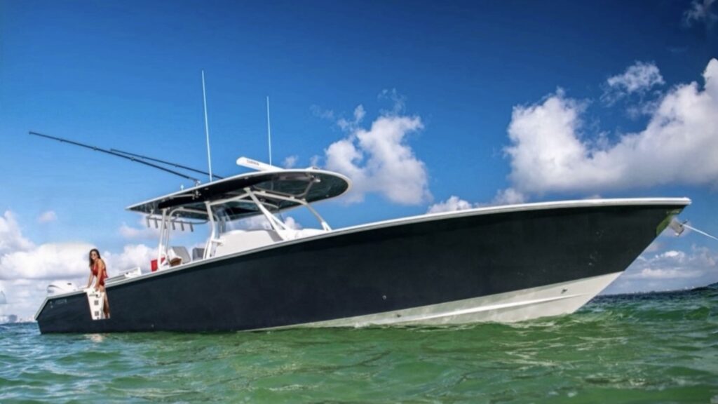 Image of a sleek, dark-colored fishing boat floating calmly in the water. A woman in a red swimsuit is standing at the stern, enjoying a sunny day under a clear blue sky with a few scattered clouds.