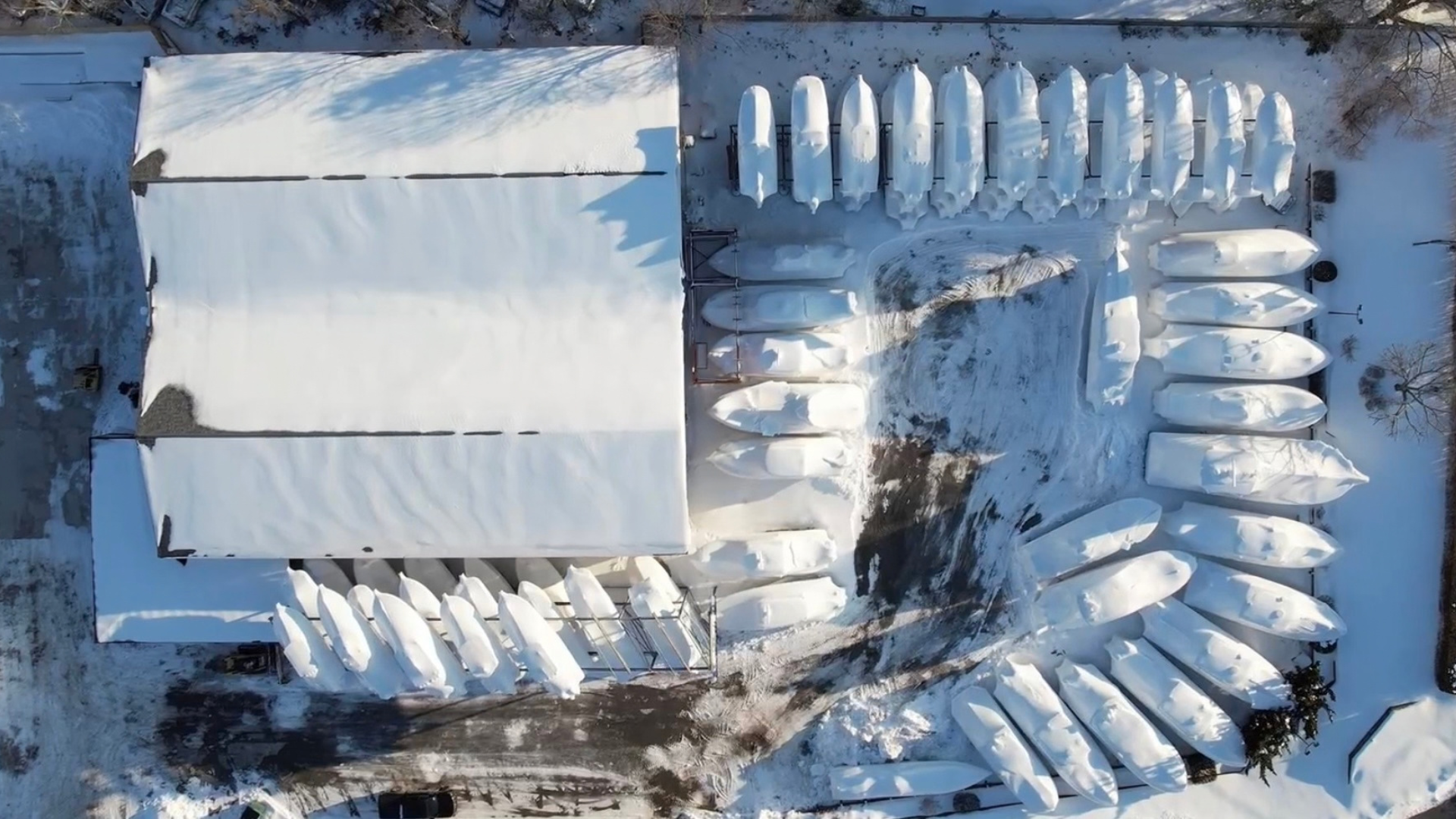 Overhead view of shrink-wrapped boats surrounding a snow-covered building at Modern Yachts, offering winter boat storage on Long Island.